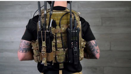 Back view of a person wearing a black shirt and tan tactical vest with rifle magazines and gear pouches