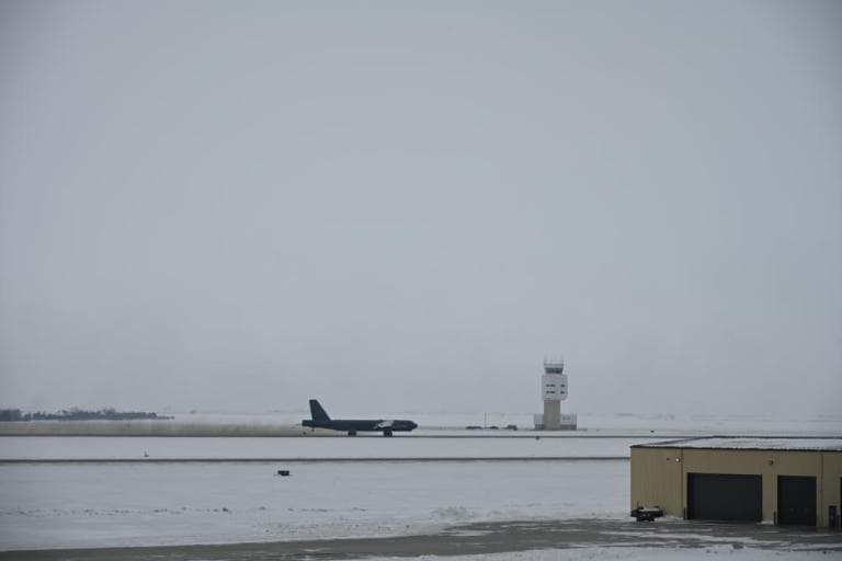 Snow-covered airfield with a small jet on the runway and a distant control tower in winter light.